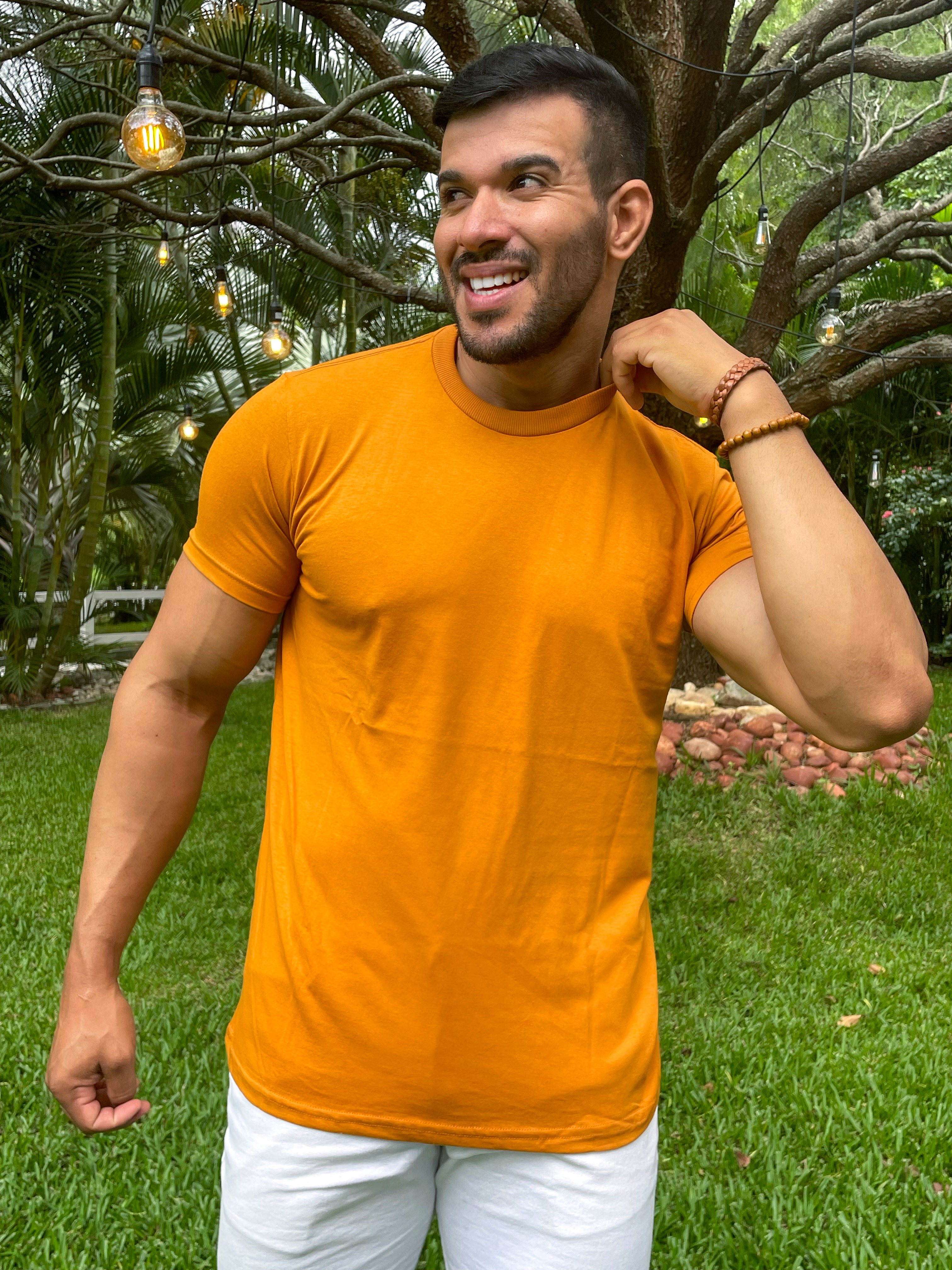 Camiseta Caramelo Homem sorrindo usando uma camiseta caramelo em um ambiente natural com árvores e grama verde.